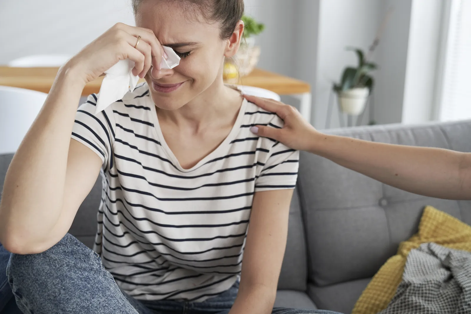 A woman crying as another person offers a comforting hand