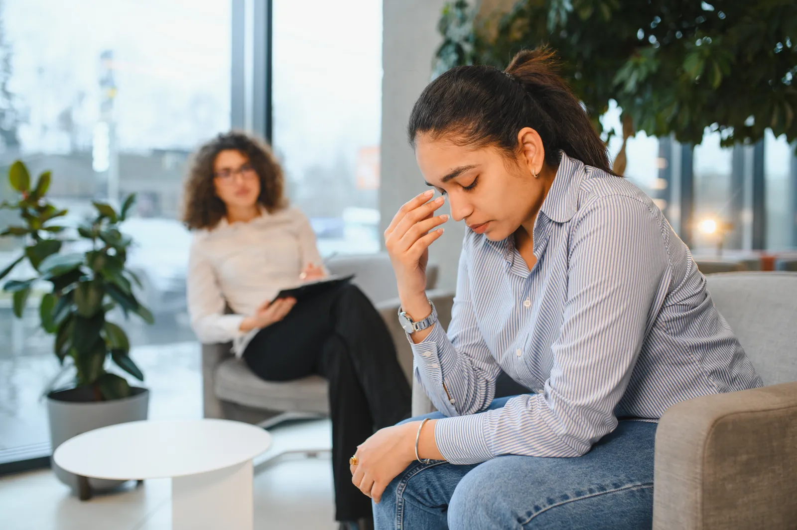 A woman speaks with another person in a light room