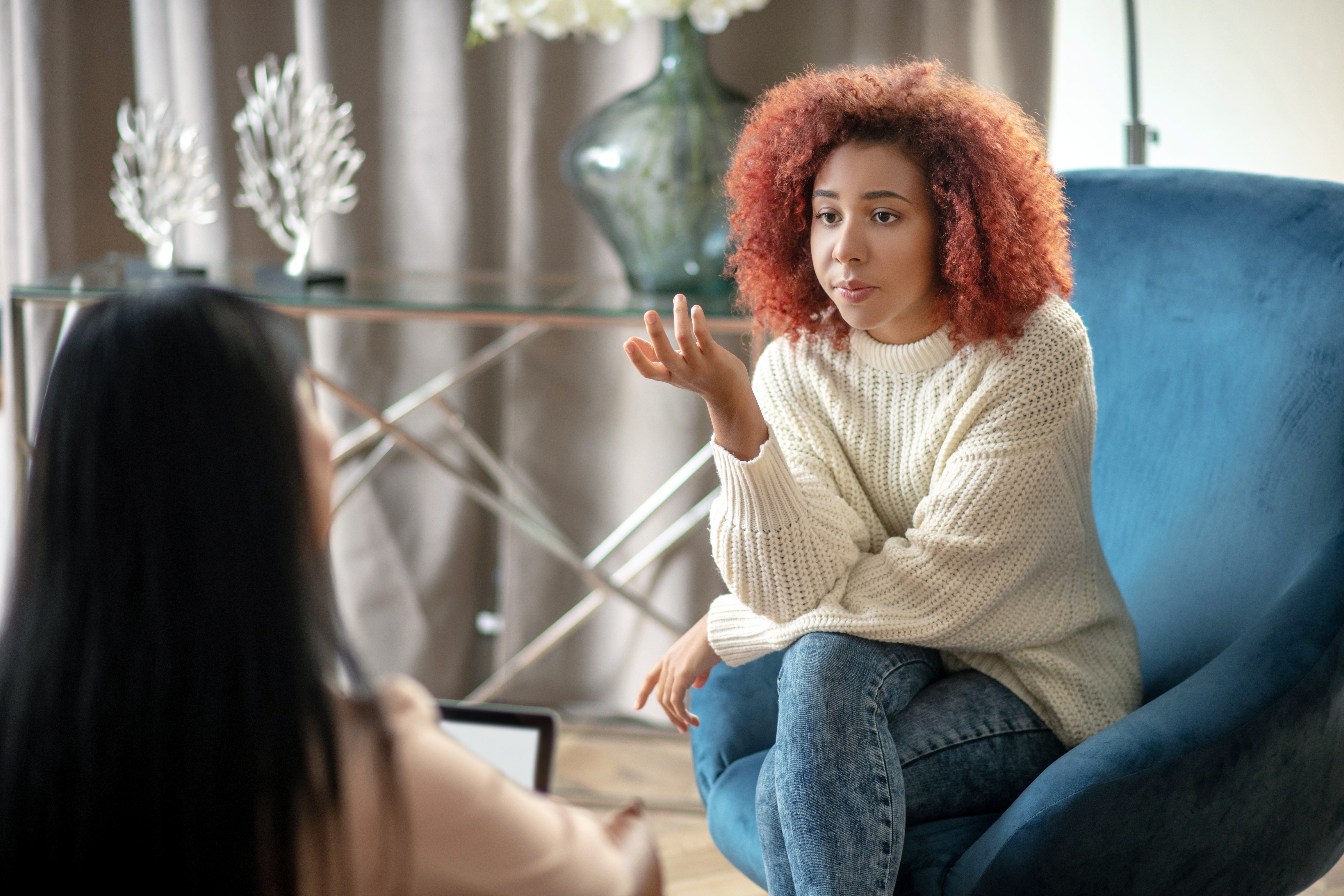 A woman speaking with a therapist in a comfortable room with a blue chair.