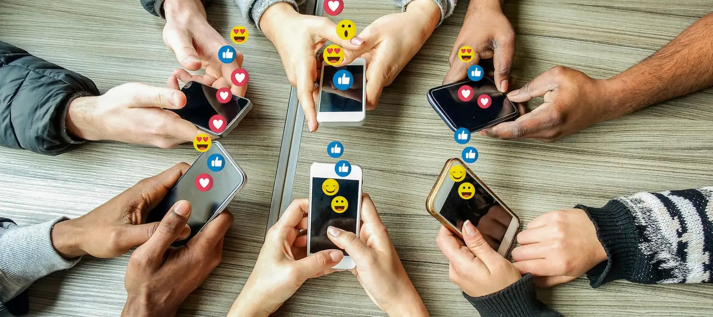 Multiple hands holding smartphones surrounded by floating social media icons — likes, hearts, and reactions