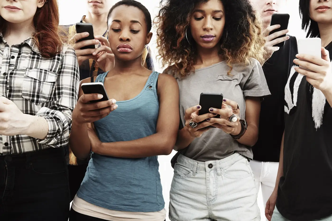 Diverse young women standing in a row, each absorbed in their smartphone screen