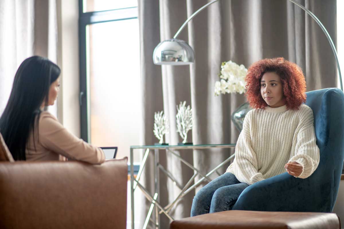 A woman in a therapy session, talking with her clinician on a sofa