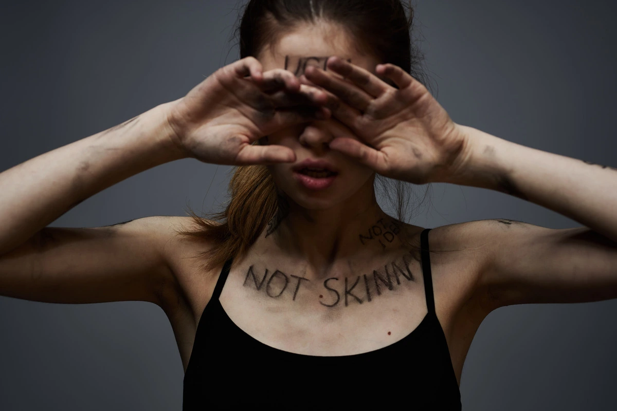 A woman crouched over a scale, hand on head — the daily weight of the disorder.
