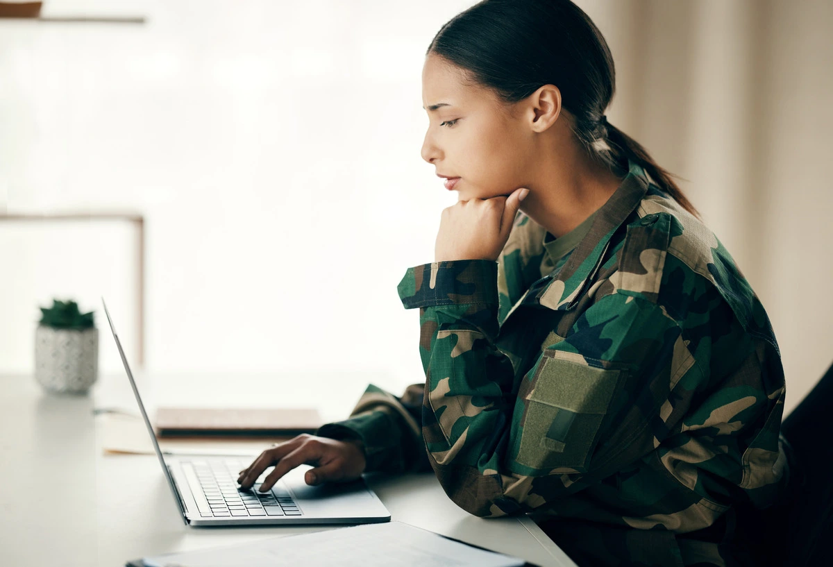 A woman in a military jacket working confidently on her laptop
