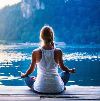 A woman sitting peacefully by a still lake, practicing mindfulness