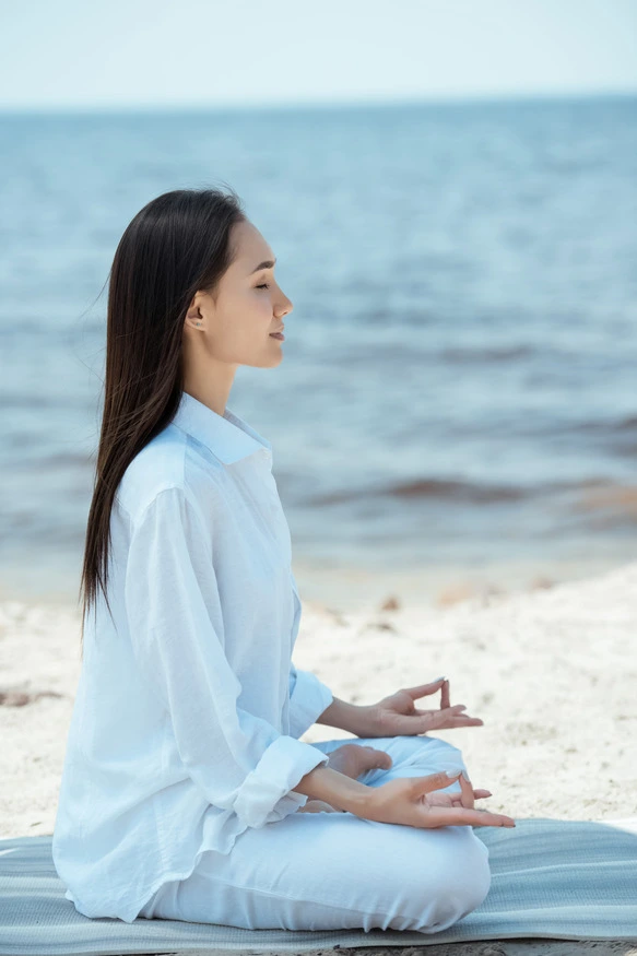 A woman meditating peacefully by the ocean — stillness and coastal healing