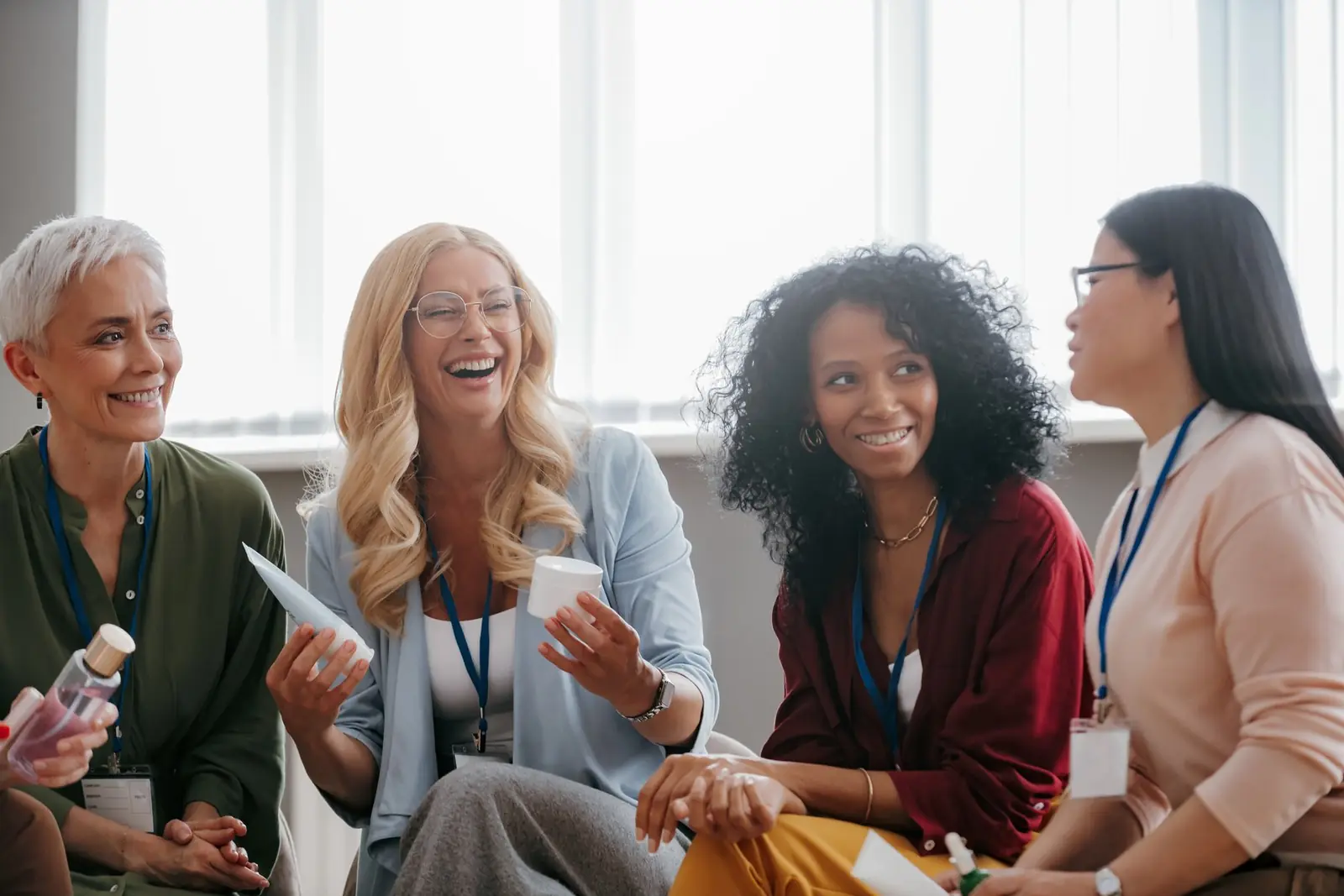 A diverse group of women laughing together in a window-lit room