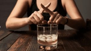 Glass of alcohol, girl making cross with fingers in front of it