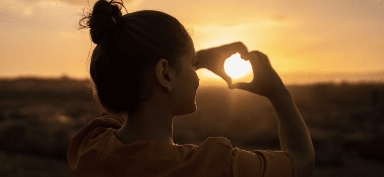 woman making a heart with her hands at the sun