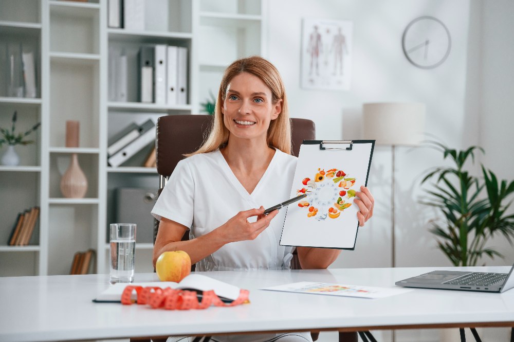 doctor in white coat is indoors with picture of food and vitamins