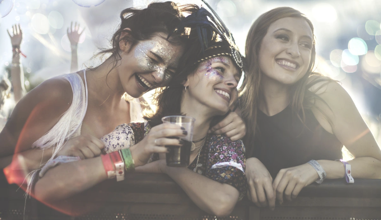 Three young women smiling together at a music festival, the kind of recreational setting where MDMA use commonly begins